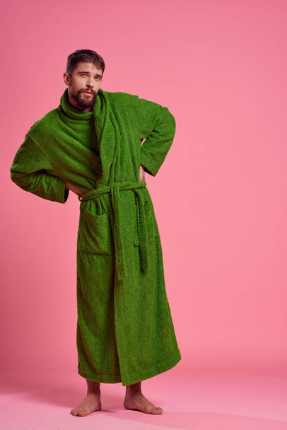 An emotional man in a green robe in full growth on a pink background gestures with his hands to the model - Foto, Imagem