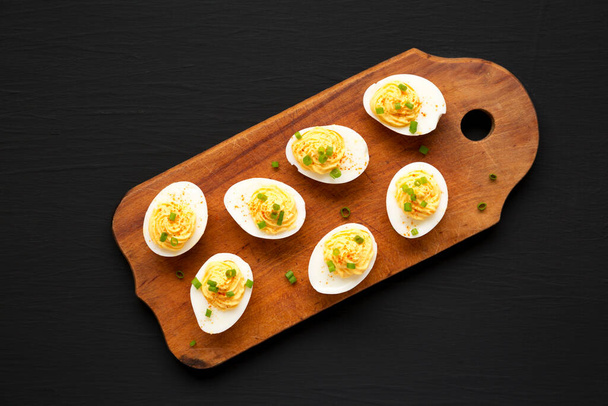Huevos hechos en casa con papas fritas en una tabla de madera rústica sobre un fondo negro, vista superior. Acostado plano, arriba, desde arriba. - Foto, imagen