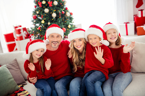 Full family x-mas dream time. People mom mommy dad daddy and little preteen kids sit sofs couch wave hands greet newyear wear santa claus cap in house indoors with christmas decoration - Фото, зображення
