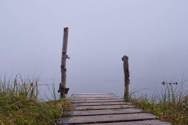 Old small jetty by a lake with fog and forest in the background - Фото, изображение