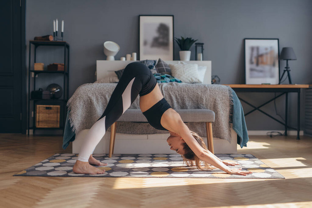 Mujer en forma haciendo ejercicio de estiramiento en la mañana en casa. pose de yoga perro orientado hacia abajo - Foto, imagen