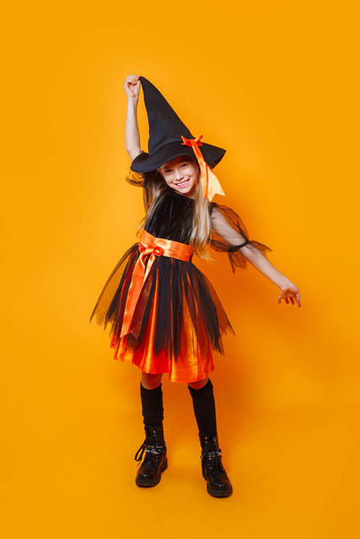 Funny little girl in witch Halloween costume on orange background - Foto, imagen