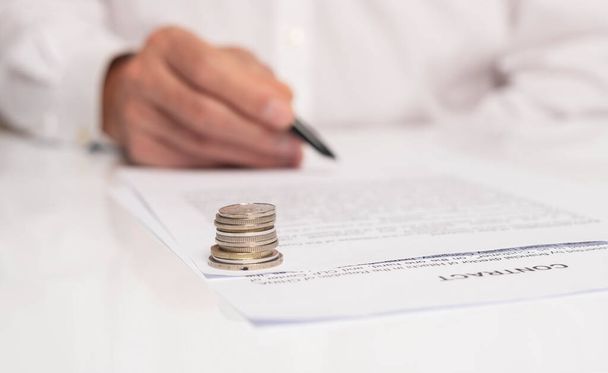 Contract signing concept. Businessman hand with pen over document closeup. money coins in focus on foreground - Fotografie, Obrázek