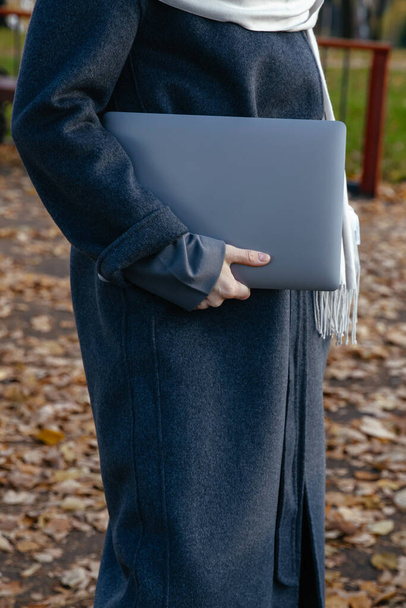 Egy kabátos lány laptopot tart a kezében a szabadban. - Fotó, kép