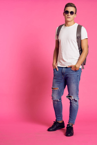 Portrait of a man in a white T-shirt and with a backpack on his back sunglasses pink background model - Photo, Image
