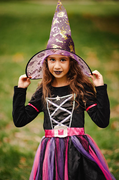 Κορίτσι με σγουρά μαλλιά σε κοστούμι μάγισσας για το Halloween σε πράσινο φόντο - Φωτογραφία, εικόνα