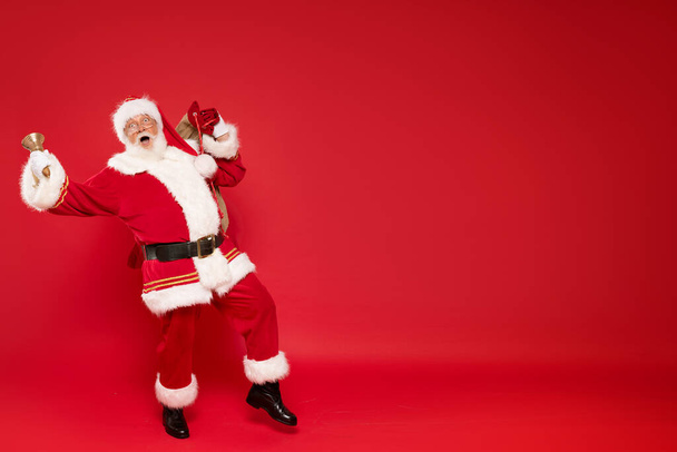 Happy, real, funny Santa Claus holding sack bag with Merry Christmas presents , delivering xmas gifts. Red background, a lot of copy space. - Foto, Bild