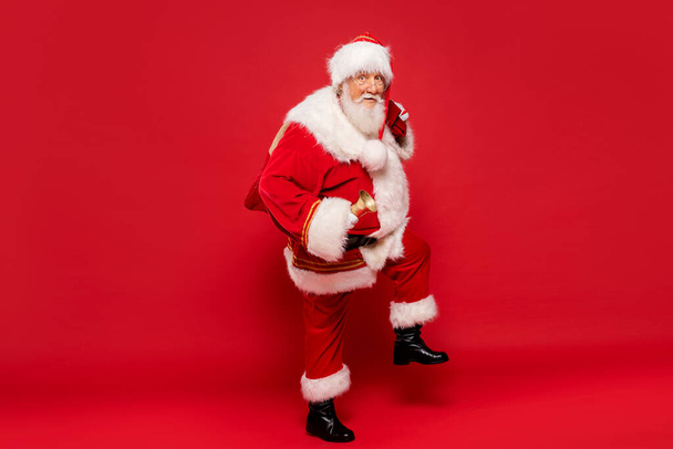 Happy, real, funny Santa Claus holding sack bag with Merry Christmas presents , delivering xmas gifts. Red background, a lot of copy space. - Φωτογραφία, εικόνα