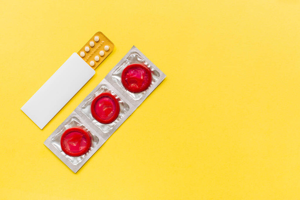 Composition with colorful condoms and birth control pills on yellow background. Safe sex and contraceptive concept. Flat lay, top view, copy space. - Valokuva, kuva