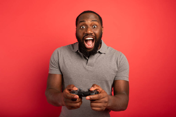 Ευτυχισμένος άνθρωπος παίζει με ένα βιντεοπαιχνίδι σε κόκκινο φόντο - Φωτογραφία, εικόνα