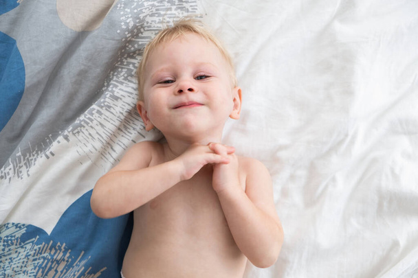 幸せな赤ちゃんの男の子はベッドと笑顔に横たわっています,上からの眺め,テキストのためのスペース. - 写真・画像