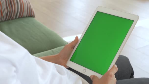 Punto de vista de la mujer india que usa gestos de mano en la computadora de tableta digital de pantalla falsa verde en modo paisaje mientras está sentada en un sofá. En el fondo acogedor salón. - Metraje, vídeo