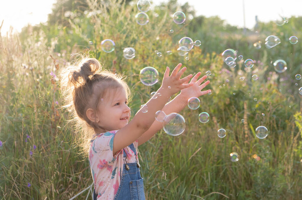 fille enfant avec queue de cheval drôle attrape bulles de savon dans la nature. - Photo, image