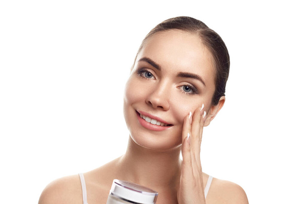 Beautiful Young Woman with Clean Fresh Skin touch own face and holds cream  moisturizing  . Facial treatment. Beauty and spa . Skin Care. Cosmetics. - Photo, image