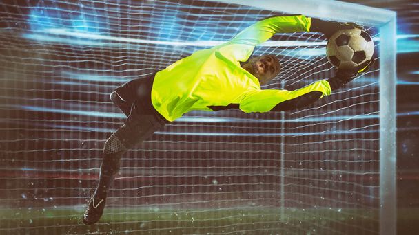 Portero de fútbol, en uniforme fluorescente, hace un salvamento y evita un gol durante un partido nocturno - Foto, imagen