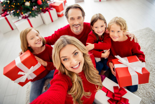 Photo of full big family five people gathering three small kids sit floor hold present box mom make shoot selfie wear red jumper in living room x-mas tree lights many gifts indoors - Foto, afbeelding