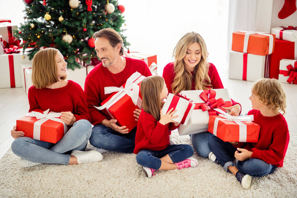Photo of full family five people gathering three small kids sit carpet exchange big boxes present wear red jumper jeans in living room x-mas tree garland many gifts indoors - Foto, imagen