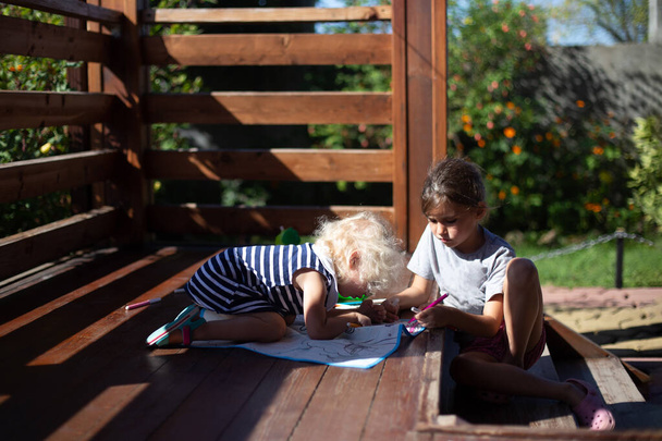 Due ragazze che disegnano sulla veranda in legno nella casa di campagna nella soleggiata giornata estiva. Cottagecore concetto estetico. - Foto, immagini