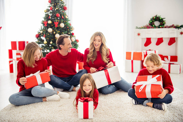 Foto di piena grande famiglia cinque persone che si riuniscono tre bambini piccoli siedono pavimento tappeto bianco ricevere regali indossare jeans maglione rosso in decorato soggiorno x-mas albero molte scatole luci all'interno - Foto, immagini