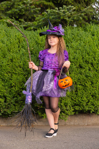 chica en un traje de bruja púrpura con calabaza naranja y escoba. - Foto, Imagen