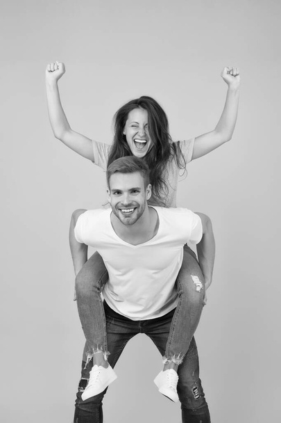 Solid support. Cheerful man piggybacking his girlfriend. Hipster giving sexy woman piggyback ride. Happy couple in love on yellow background. Loving couple smile having fun. Simple happiness - Фото, изображение