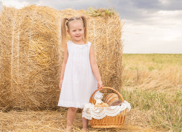 niña rubia en vestido de algodón blanco sosteniendo cesta de pan. - Foto, imagen