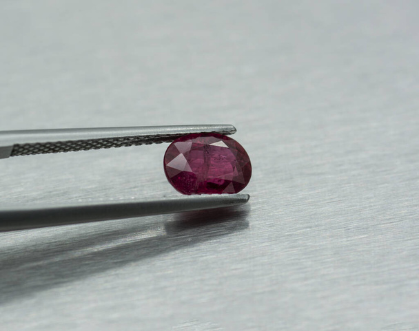 Preciosa piedra de rubí tallada y sujeta con pinzas sobre fondo metálico - Foto, Imagen