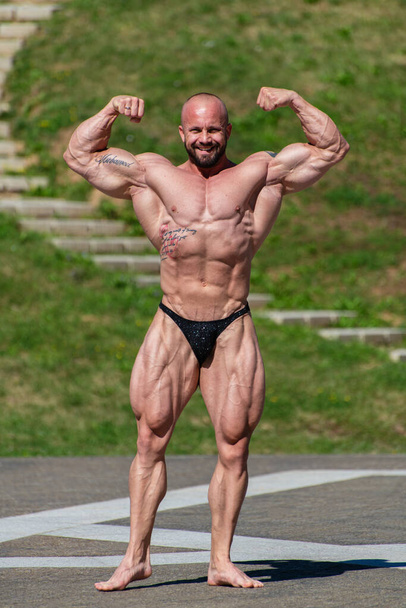 Powerful muscular bodybuilder in panties posing at the park. Quadriceps and upper body contraction - Φωτογραφία, εικόνα