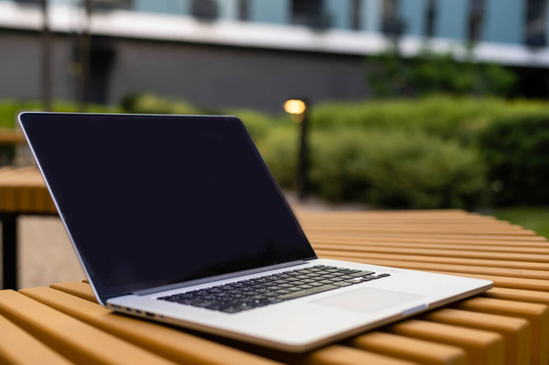 Een laptop met leeg scherm staat op een houten bankje op de binnenplaats, werkruimte van freelancer in een prachtige huistuin - Foto, afbeelding