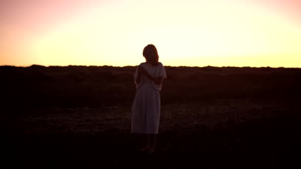 Una joven mujer caucásica está de pie en un campo ang alejándose después de haber comprobado su teléfono inteligente - Imágenes, Vídeo