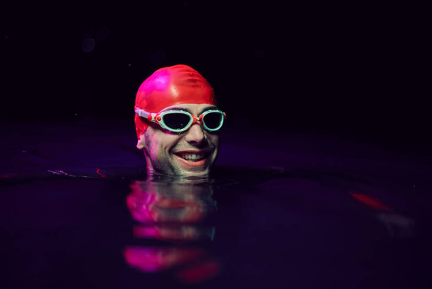 authentic triathlete swimmer having a break during hard training on night neon gel light - Foto, Imagem