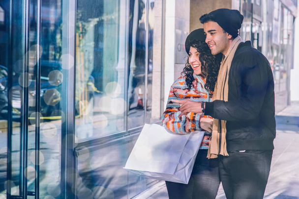 Milenial sonrisa masculina y femenina durante las compras durante las vacaciones - Temporada de invierno - Frío - Luces - Foto, imagen