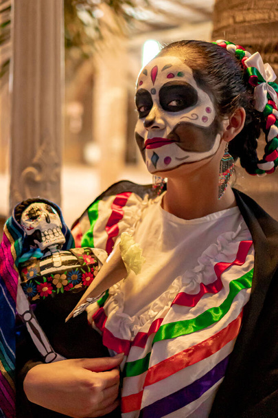 Geleneksel ölü makyajlı Meksikalı kadın elinde Meksika kostümlü geleneksel bir Meksika kafatası tutuyor.. - Fotoğraf, Görsel