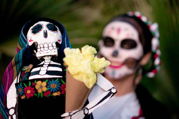 Mexican woman with colorful traditional Day of the Dead makeup holding a traditional Mexican skull with Mexican costume. - Photo, Image