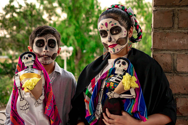 Twee tieners dragen traditionele Day of the Dead make-up, met traditionele Mexicaanse schedels met een boom achtergrond. - Foto, afbeelding