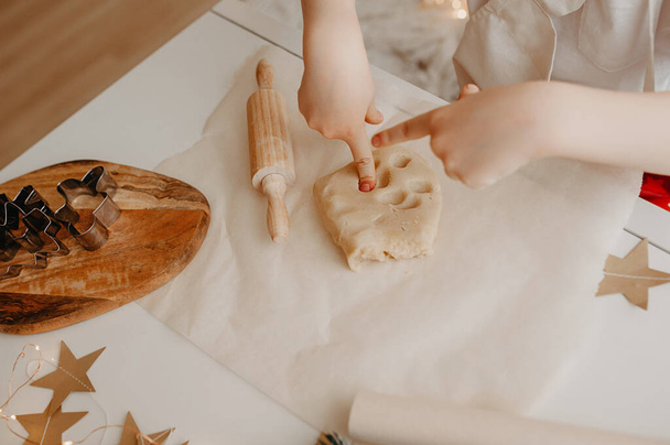 дитина штовхає пальці в тісто, готуючи домашнє печиво, використовуючи дерев'яний штифт, металеві форми для печива на папері для випічки
 - Фото, зображення