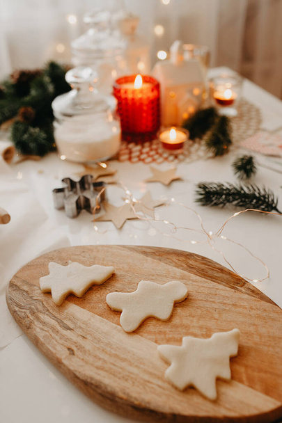 biscotto crudo sotto forma di albero di Natale, fiocchi di neve e un uomo su una tavola di legno sullo sfondo di decorazioni natalizie, candele ardenti e ghirlande - Foto, immagini
