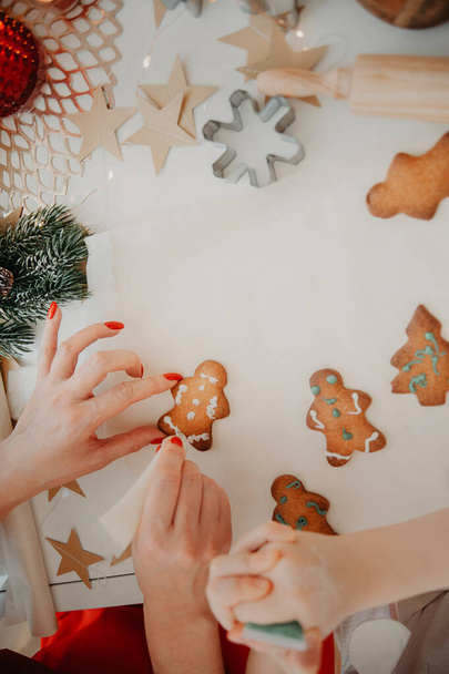 las manos de mamá y el bebé cortan galletas de la masa usando moldes metálicos, sobre papel de hornear, sobre una mesa blanca con decoración de estrellas de papel - Foto, imagen