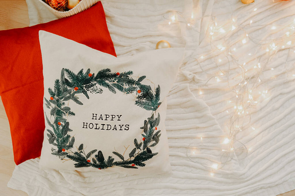 λευκό τόξο με χριστουγεννιάτικο δέντρο διακόσμηση και χαρούμενες διακοπές pises σε ένα λευκό καναπέ με ένα θολό χριστουγεννιάτικο δέντρο και bokeh φώτα στο παρασκήνιο - Φωτογραφία, εικόνα