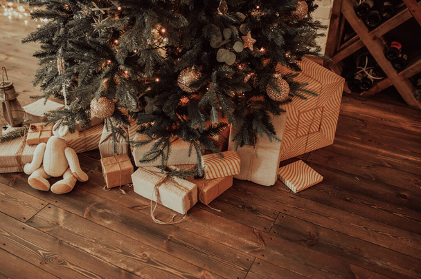 φιλικά προς το περιβάλλον κουτιά δώρων σε επαναχρησιμοποιήσιμη υφασμάτινη συσκευασία και κορδέλα, σε μεγάλους αριθμούς κάτω από το χριστουγεννιάτικο δέντρο σε σκούρο ξύλινο παρκέ - Φωτογραφία, εικόνα