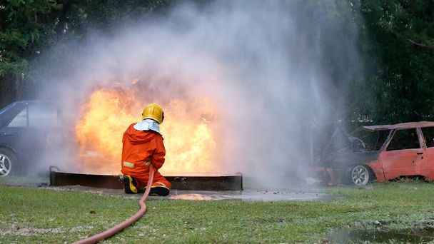 Пожарный борется с пламенем с помощью пожарного шланга химического распылителя воды. Пожарный носит каску, костюм для защиты. Спасательные учения на огнетушителе - Фото, изображение