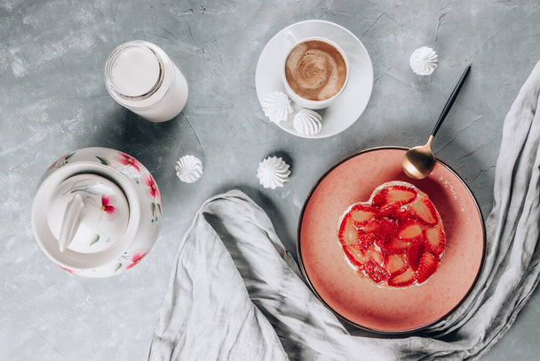  Cup of coffee, cake with strawberries, milk and meringues on a gray table, top view. High quality photo - Foto, imagen