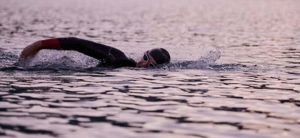 triathlon athlete swimming on lake in sunrise wearing wetsuit - Foto, immagini