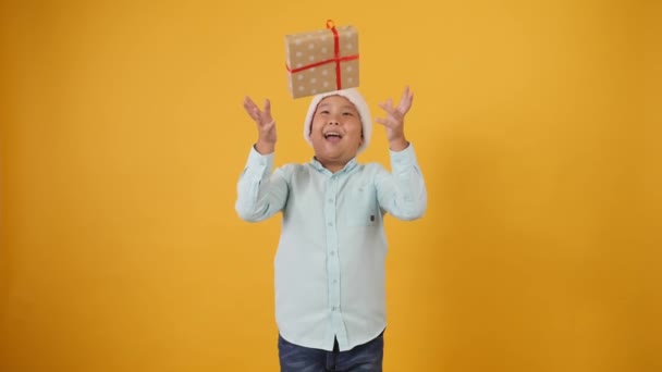 Funny Asian boy in Santa hat throwing his Christmas gift on color background - Imágenes, Vídeo