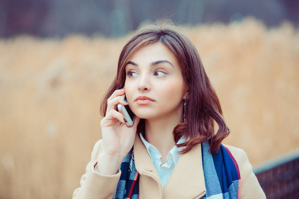 Skeptical woman talking on phone deciding what to answer outdoors park in autumn on background - Foto, Imagen