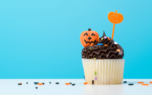 Halloween Cupcake. Cupcake dessert decorated with chocolate cream, candy shaped pumpkin Jack-o-lantern frosting or Icing. Cupcakes on blue background. Happy Halloween!!! - Photo, Image