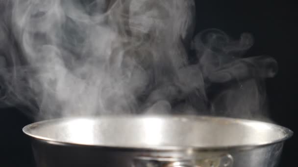 Stoom- of dampwolken die ontstaan uit een kokende stalen koekenpan op het fornuis. Stoom tijdens het koken uit de pan. Koken in slow motion. Stoom en witte rook stijgen op zwarte achtergrond. Vol hd - Video