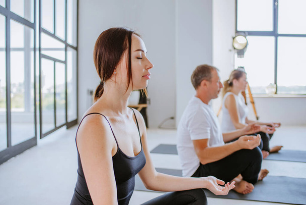 Молодая женщина в классе йоги медитирует с закрытыми глазами - Фото, изображение