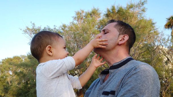 Junger kaukasischer Vater hält sein Kleinkind. Baby berührt das Gesicht seines Vaters - Foto, Bild