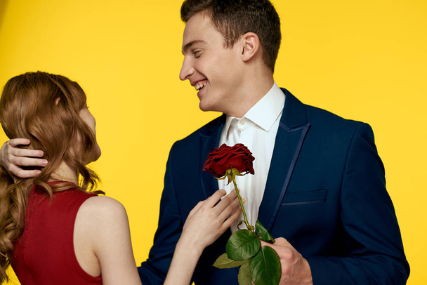 коханці чоловік і жінка з червоною трояндою в руках обіймаються на жовтому фоні романтичні відносини любов сім'я
 - Фото, зображення